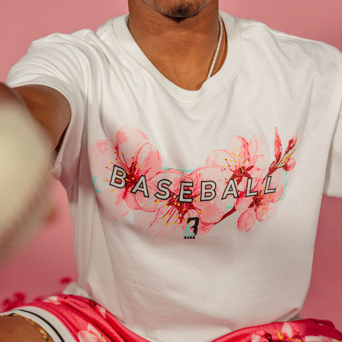 Close up of the cherry blossom Baseball graphic on a white BL101 tee worn by a male model against a pink background