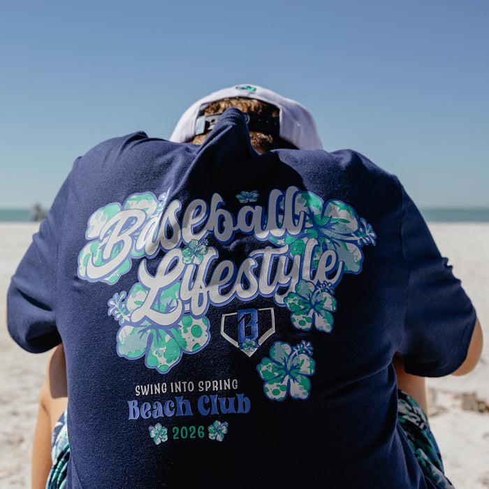 Person wearing a navy blue shirt with 'Baseball Lifestyle Swing into Spring Beach Club 2026' text and floral designs on a beach