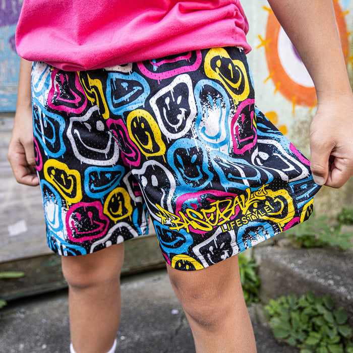 Youth model wearing multi-color youth shorts with “Smiley Slugger” design