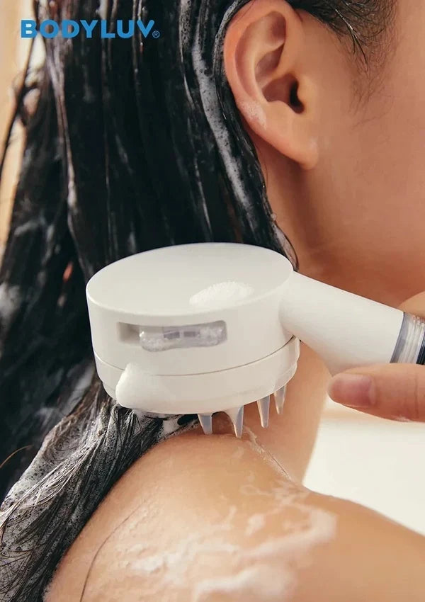 A close-up of a person receiving a neck and shoulder scalp massage treatment with a white handheld device branded BODYLUV. The person has wet, dark hair, and the device is shown applying pressure with soap lather on the skin.