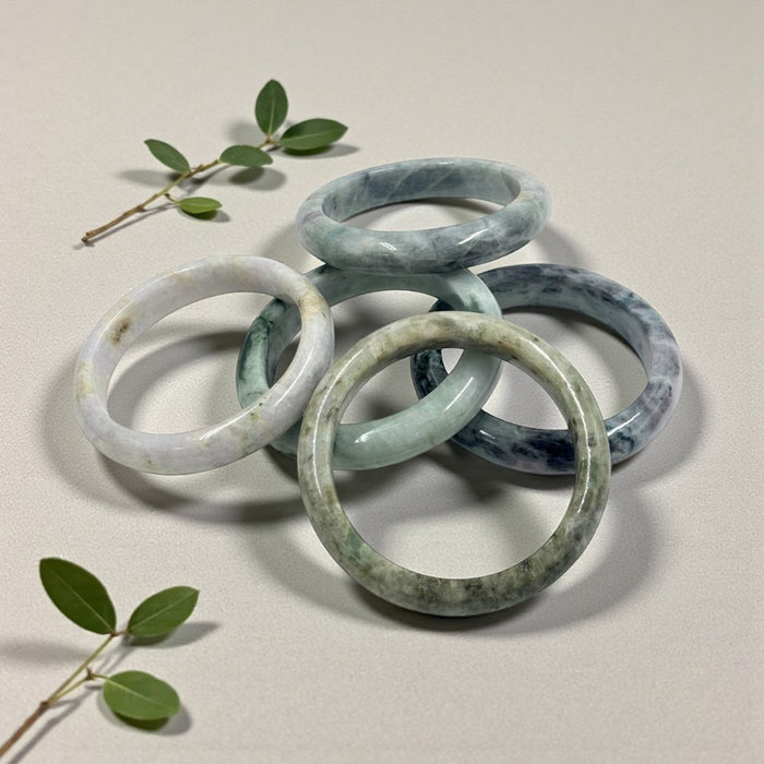 Stack of jade bracelets on a light background with green leaves.