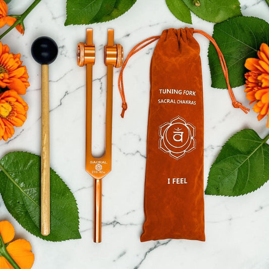 Tuning fork and mallet with a drawstring bag on a marble surface with flowers and leaves.