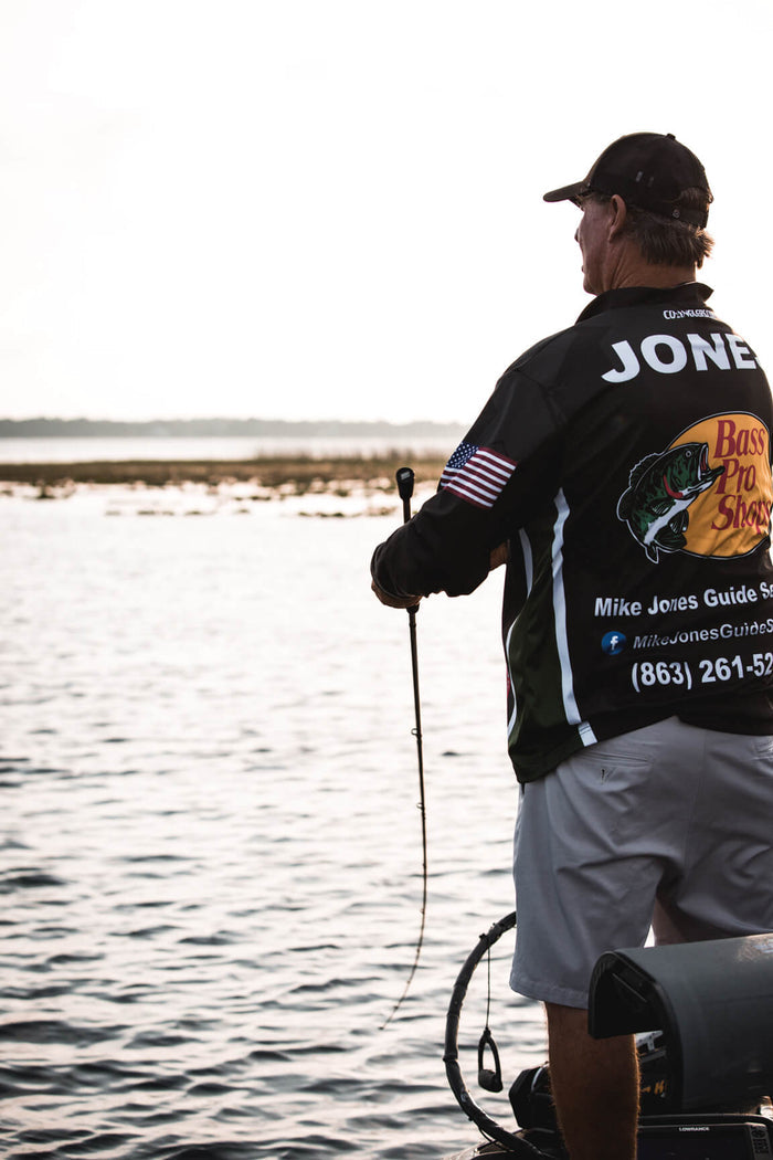 A fisherman is standing on a boat and reeling in his line.