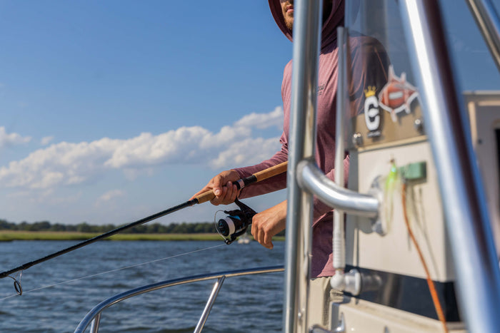 There is a fisherman standing on a boat and holding onto a fishing pole.