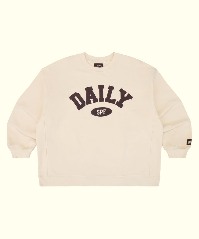 An off-white crewneck sweatshirt featuring a dark brown graphic on the chest that reads 'DAILY SPF' with 'SPF' inside an oval. A small brand tag is visible on the left sleeve cuff, and the inner collar shows the brand name 'DAILY'.
