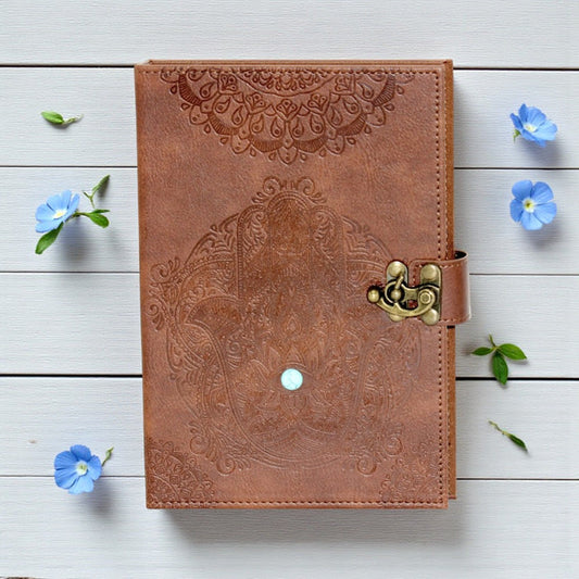 Brown leather notebook with embossed design and gold latch on a light wooden surface with blue flowers.