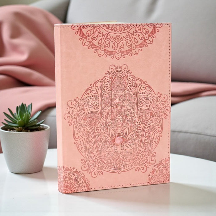 Pink Hamsa Journal on a white surface with a plant in the background