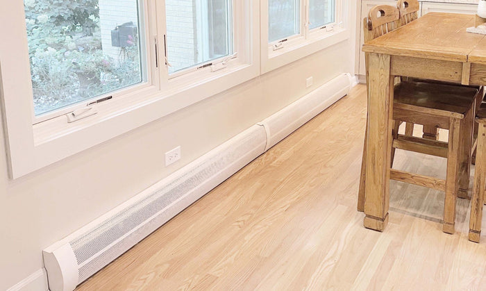 Sleek white Elliptus Series curved galvanized steel baseboard heater cover running along a bright dining room wall.