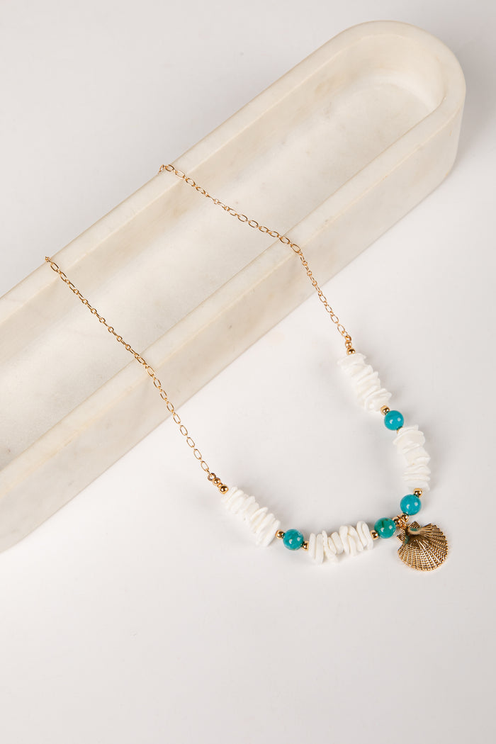 Necklace with white beads, turquoise stones, and a gold shell pendant on a marble surface.