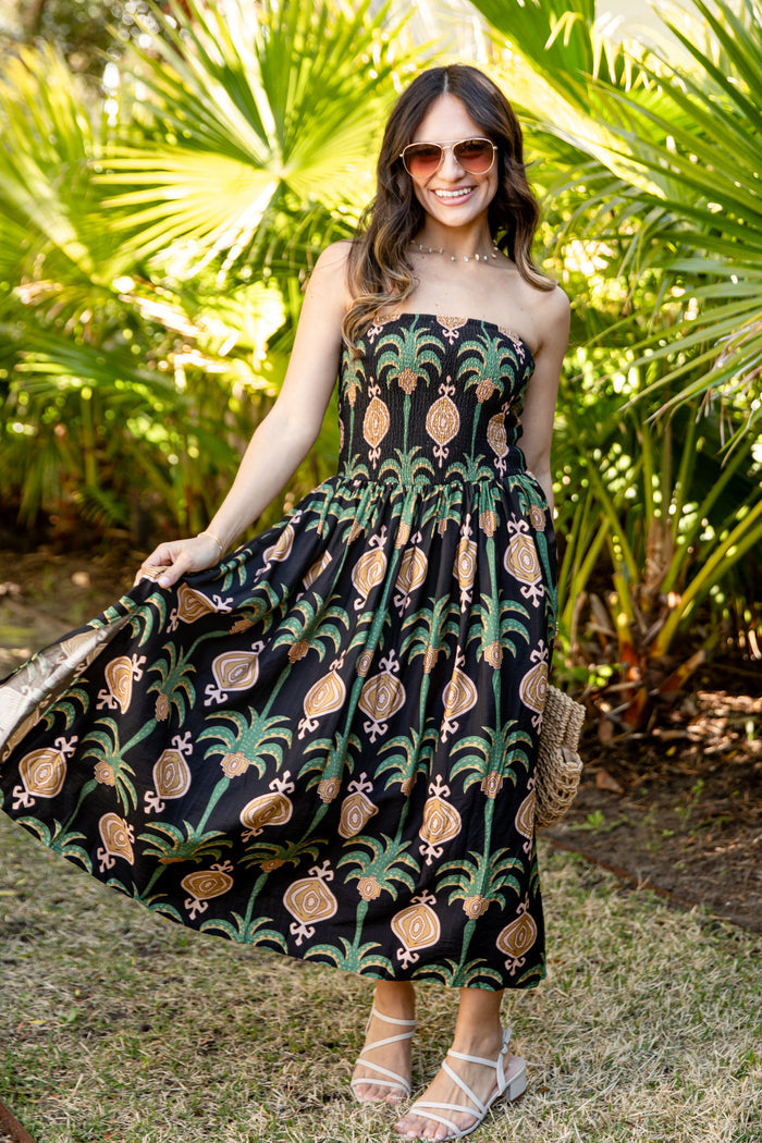 Woman in a strapless dress with pineapple pattern standing in a garden.