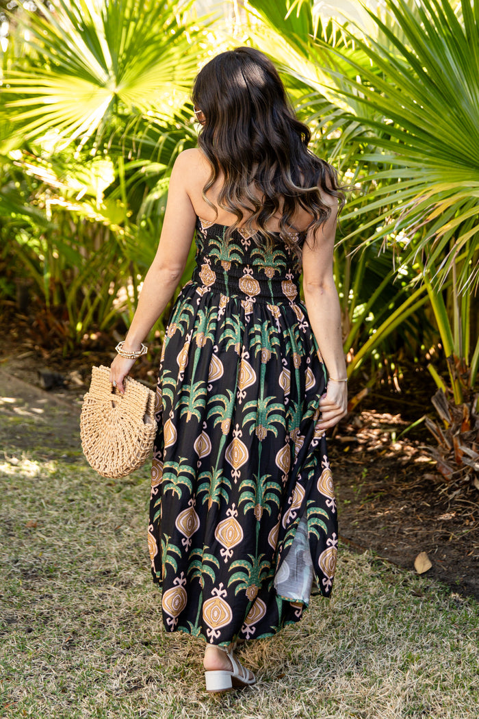 Woman in a tropical patterned dress standing in a garden with palm trees.