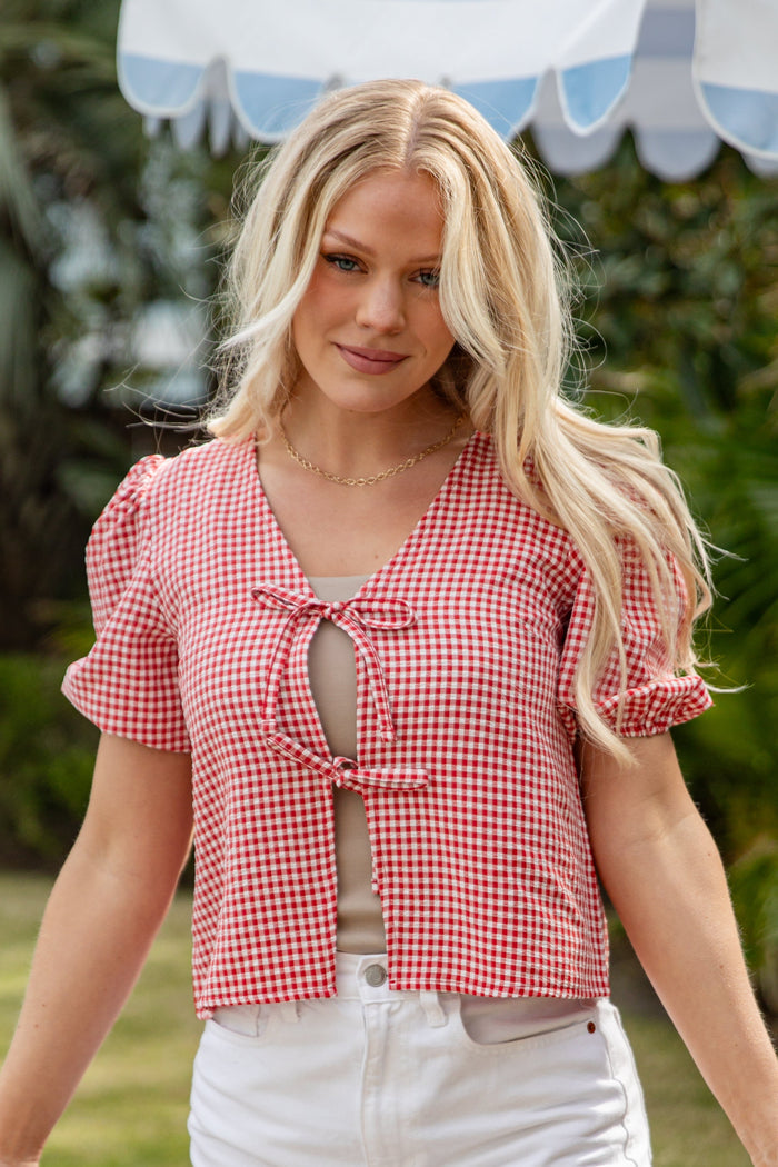 Woman wearing a red checkered top outdoors under a striped umbrella.