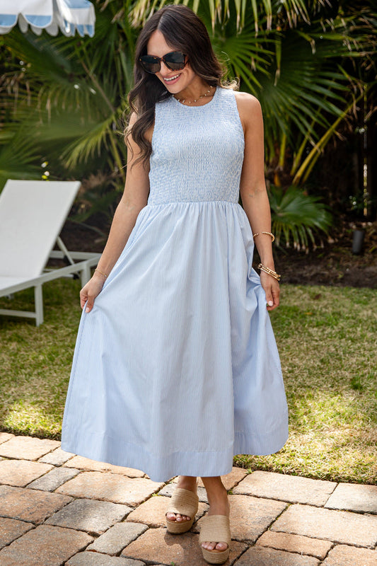 Woman in a light blue dress standing outdoors with palm trees in the background