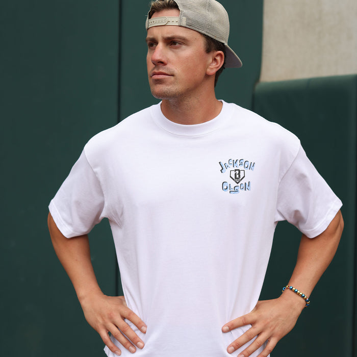 Adult male model wearing the white Jackson Olson x BL101 relaxed tee, showing the chest logo with "Jackson Olson" text and BL101 shield graphic