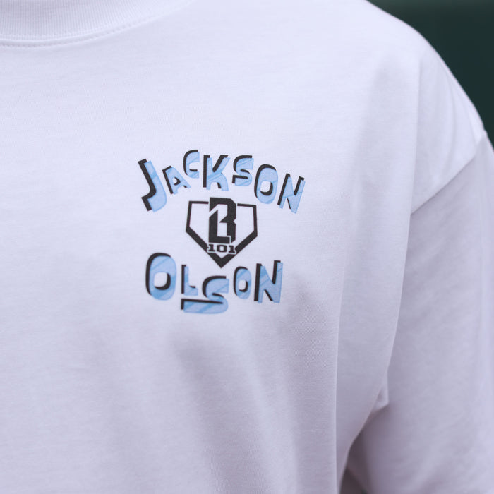 Close-up of the Jackson Olson x BL101 chest graphic on the white tee, featuring blue and black lettering around the BL101 home plate shield logo