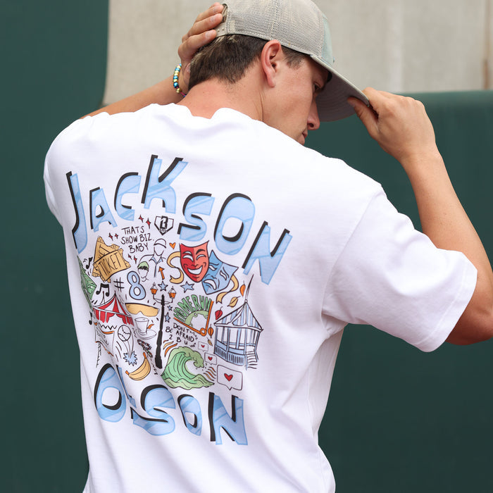 Back view of the white Jackson Olson x BL101 relaxed tee showing the large "Jackson Olson" graphic with colorful illustrated artwork and "That's Show Biz, Baby" text