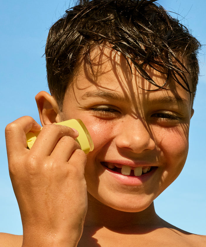Child holding a yellow object to their ear against a clear blue sky