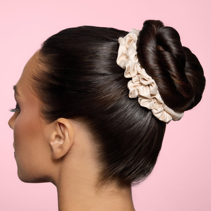 Side profile of a model with sleek dark hair in a twisted bun, secured by large champagne satin scrunchie
