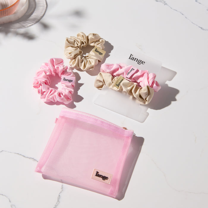pink and champagne L’ange satin scrunchies on a vanity beside a small pink zip pouch
