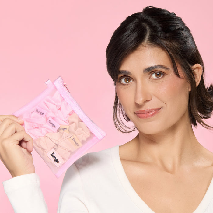 Model holding a pink mesh pouch filled with blush and champagne L’ange satin scrunchies