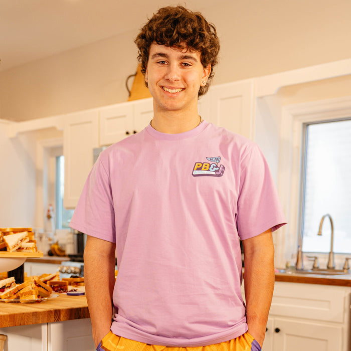 Male model smiling in a kitchen wearing the BL101 PB&J Baseball Lifestyle purple tee.