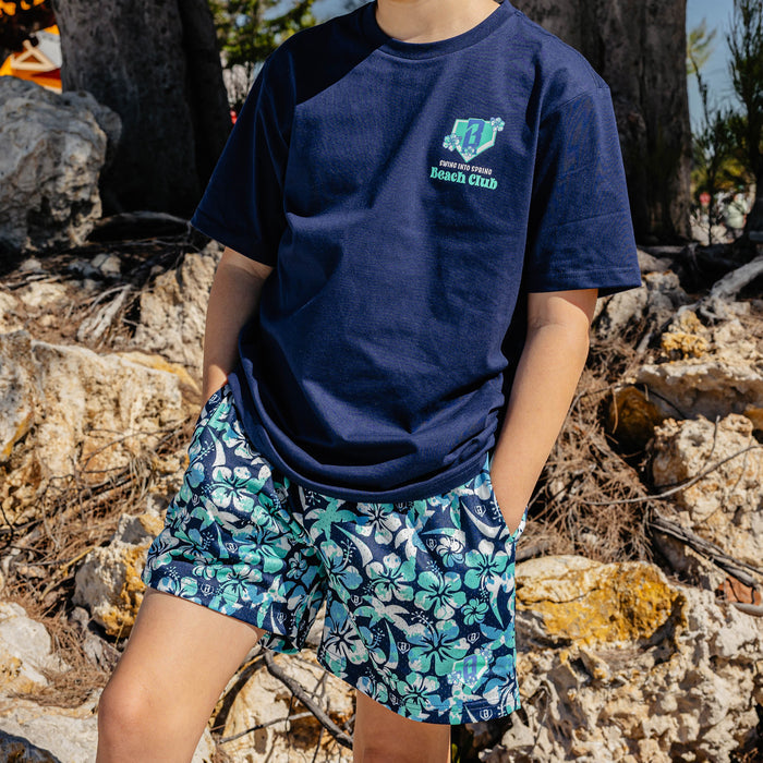 Person wearing a navy blue t-shirt with a floral BL101 logo and blue floral shorts standing on rocky terrain.