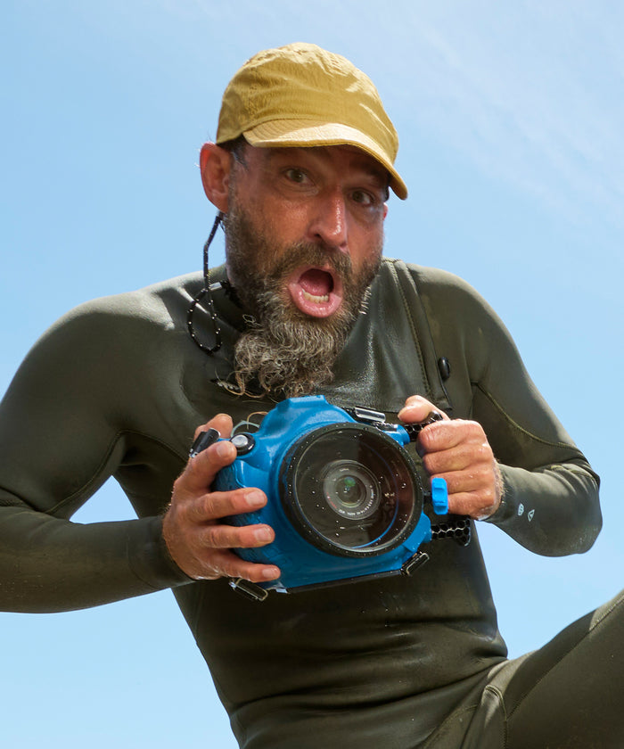 Man in wetsuit holding a blue camera against a clear blue sky