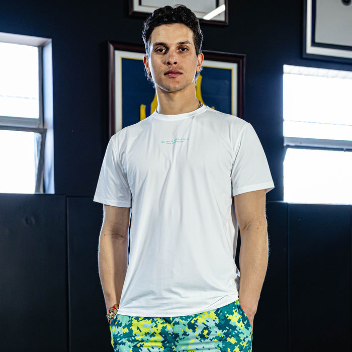 Person wearing a white t-shirt and colorful pants standing in a room with blue walls and framed pictures.