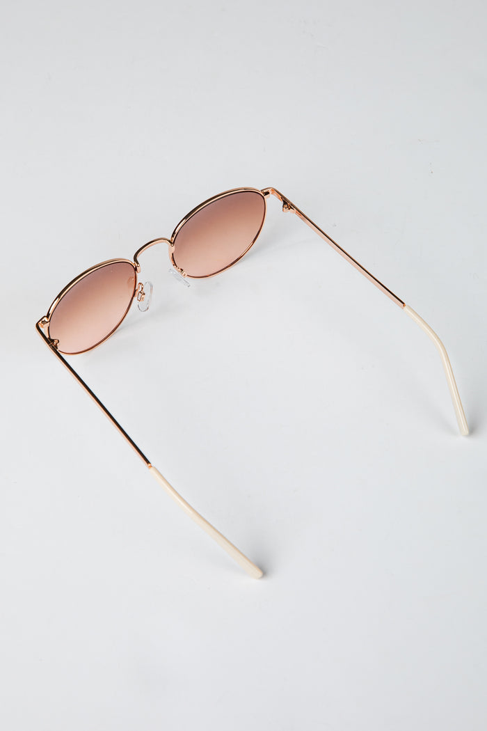 Rose gold sunglasses with pink lenses on a light gray background