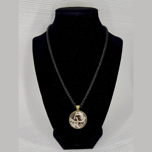 Fort Denaud Beard and Skin round pendant necklace with a textured pattern in a bronze frame on a black braided cord