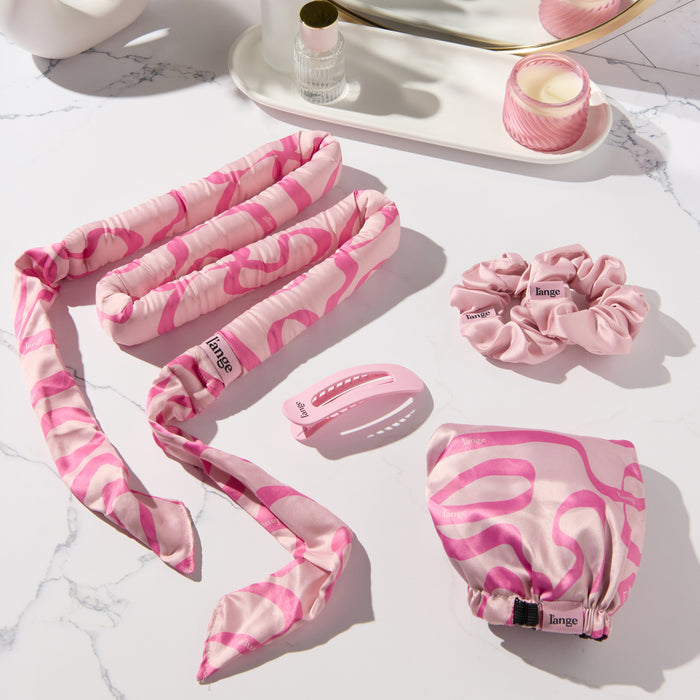 Satin Heatless Curls Set on a vanity.  Set includes a satin curling rod, an adjustable bonnet, two satin scrunchies, and a hair clip