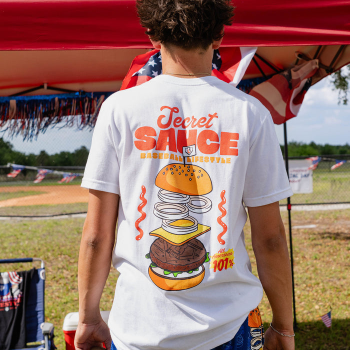Person wearing a white t-shirt with a burger graphic and 'Secret Sauce' text, standing outdoors.