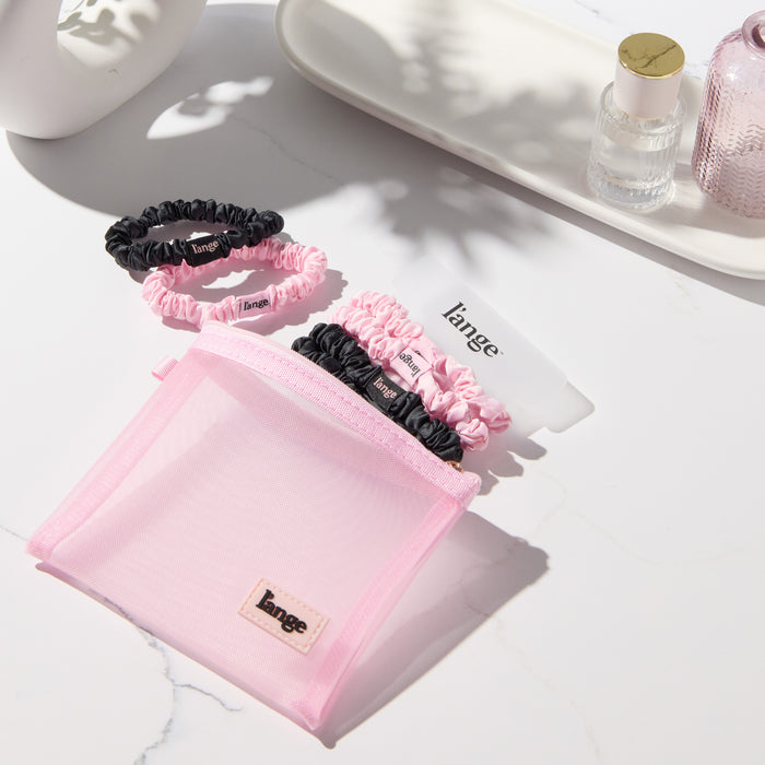 blush and black L’ange satin scrunchies on a vanity beside a small pink zip pouch