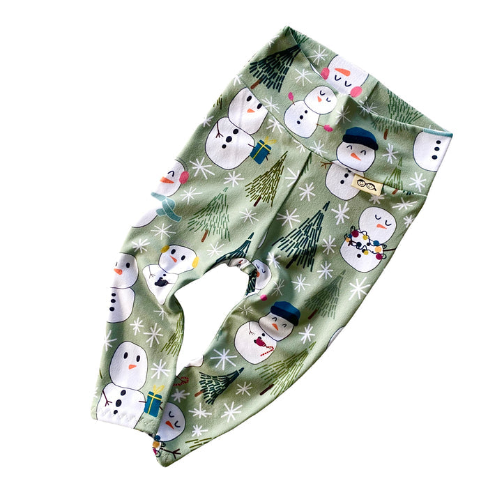 Snowman Print Leggings featuring a festive design of snowmen and winter trees on a soft green background. Handmade high-waisted leggings for babies and toddlers, perfect for holiday celebrations and seasonal outfits.