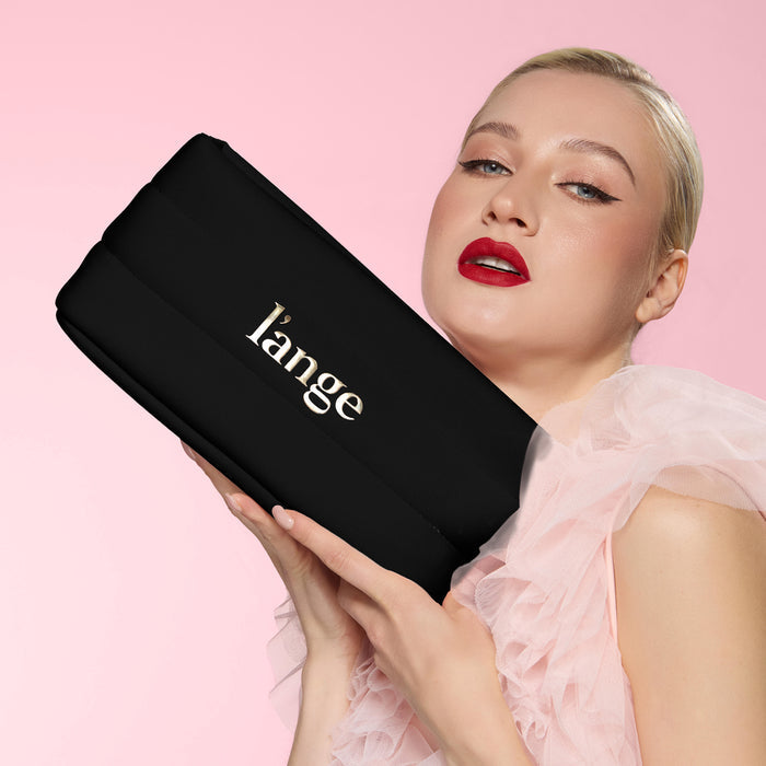 Model holding a black L’ange bag against pink backdrop