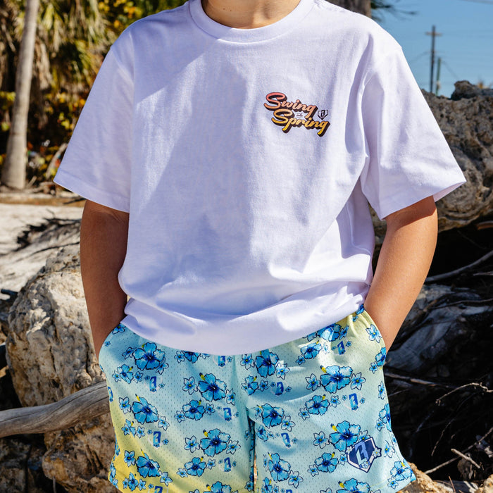 Person wearing a white t-shirt with 'Swing into Spring' text and blue floral shorts outdoors.