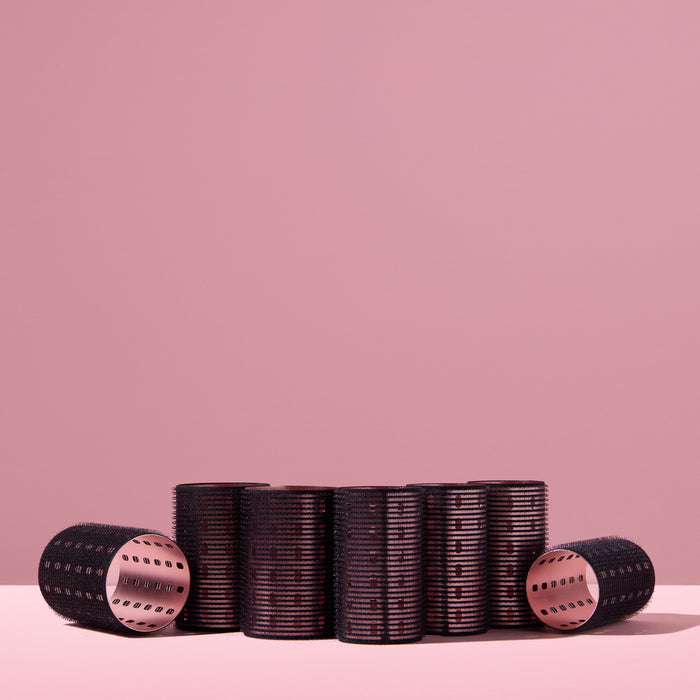 A collection of black thermal hair rollers, arranged on a pink background