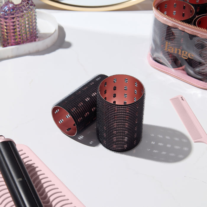 A collection of black thermal hair rollers, arranged on a white marble vanity