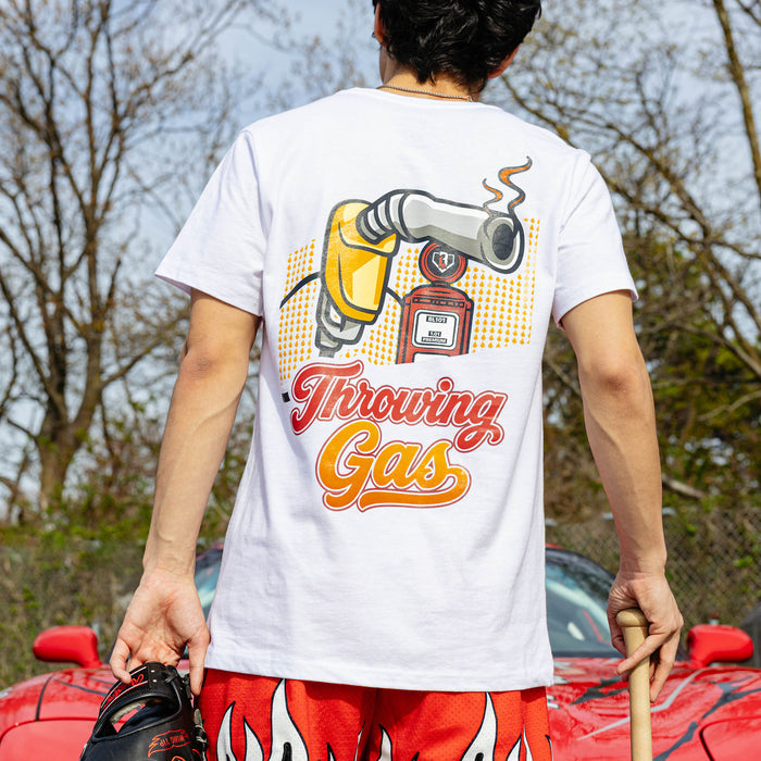 Back view of white Throwing Gas tee showing colorful gas nozzle and pump illustration, model holding glove and bat beside red car.
