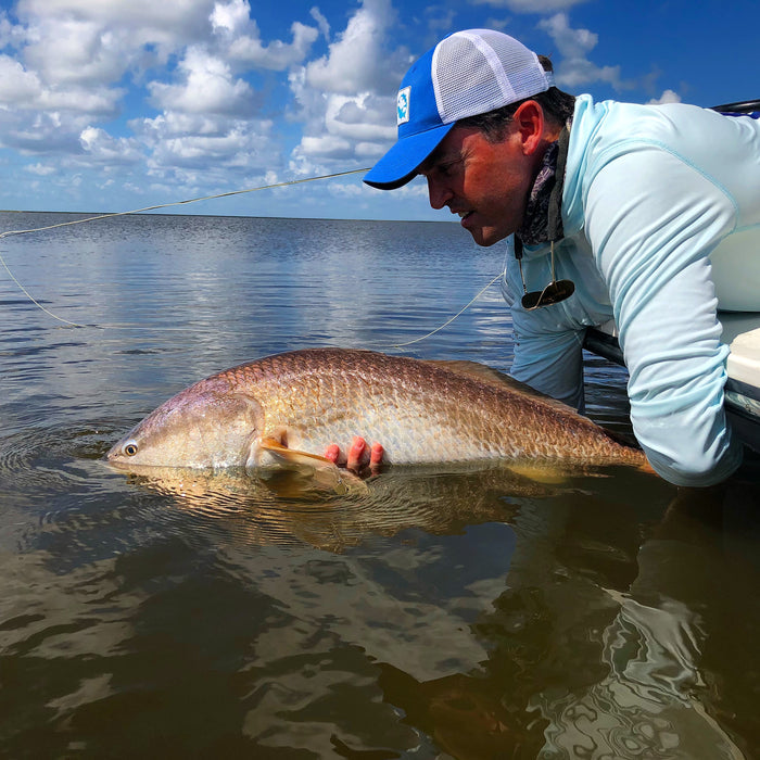 A man is leaning over a boat and holding onto a redfish in water.